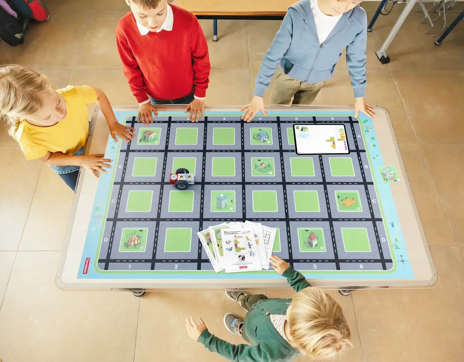 Schülerinnen und Schüler stehen um die „Wege programmieren“ Spielmatte für die Grundschule.